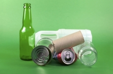 A glad bottle, tin can, soda can, glass bottle, and milk jug sit on a green background to illustrate examples of recyclable items.