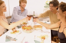 A group of four friends seated around a table with food clink their wine glasses together in celebration.