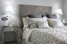 An attractive bedroom with a well-made bed with a grey headboard, mirrored side table, and matching table lamps.