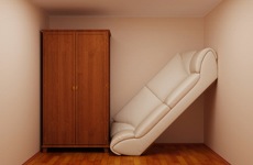A white leather couch is propped against a wooden wardrobe to illustrate that these two large furniture items cannot both fit in a small apartment space.
