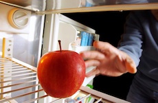 Man reaching into a refrigerator to grab a red apple. 