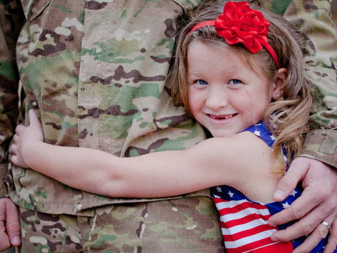 Young girl in patriotic dress hugging her father, a member of U.S. Armed Forces
