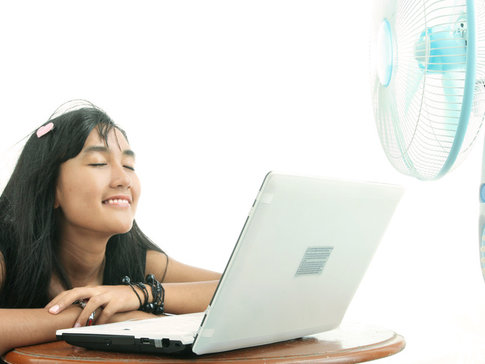 Woman relaxing on table in front of computer, as fan blows cool air on her face