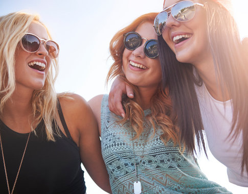 Smiling group of three girls, all stylishly dressed and wearing sunglasses