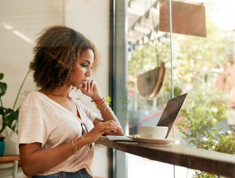 African American woman searching for short-term apartment lease on computer in trendy coffee shop
