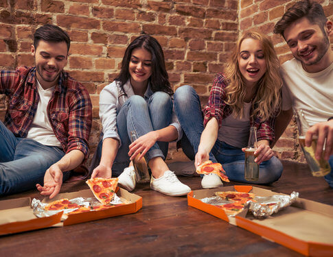 Four young college kids enjoying two boxes of pizza on the floor of an empty apartment