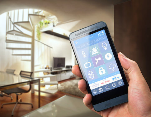 Man in apartment holding smartphone, with smartphone screen showing various ways to control the apartment's lighting, technology, A/C etc.