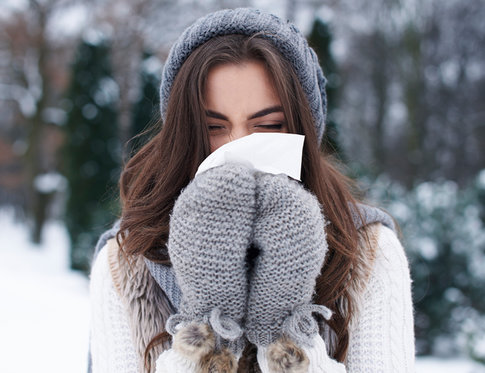 Girl in grey winter hat and mittens, outside in snow, blowing her nose