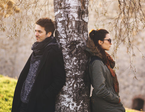 Girlfriend and boyfriend facing away from each other with backs against a tree, breaking up
