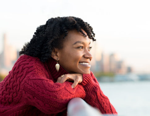 African American woman in red sweater looking out over an expanse of water, hopeful for the new year