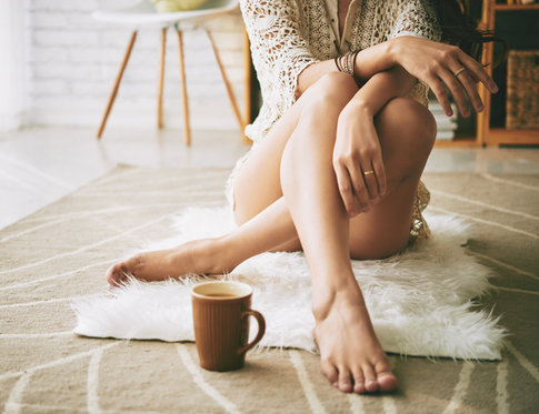 Legs of woman sitting on the floor with cup of coffee