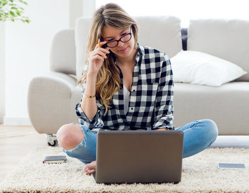 Woman sitting on shag rug in stylish apartment, writing a notice of intent to vacate on her laptop
