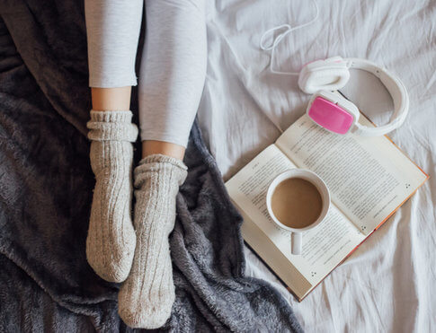 Woman's feet in cozy socks next to open book, cup of coffee, and white headphones