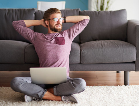 Happy man, feeling good vibes, sitting on floor of apartment with computer in lap