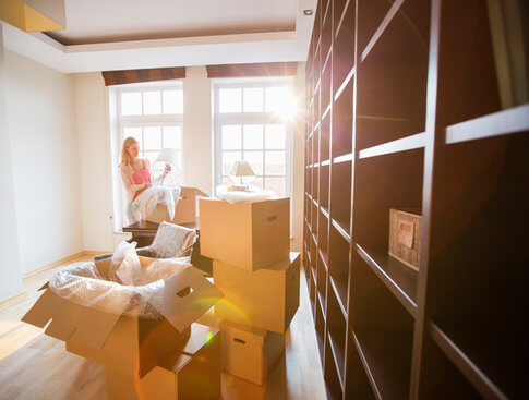 Woman unpacking in her new apartment with the sun shining brightly through the windows behind her