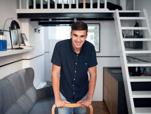 Portrait of a handsome young man smiling and leaning on a chair while standing in his modern loft apartment