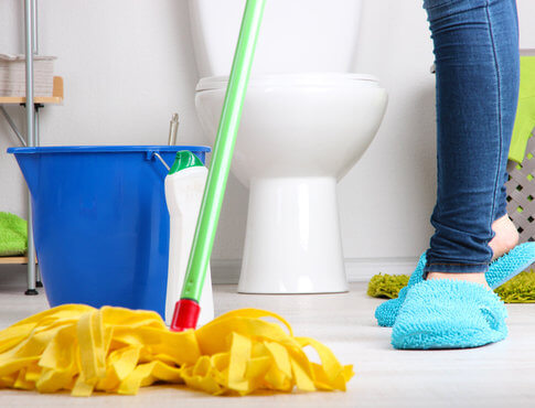Girl in blue slippers cleaning apartment bathroom floor with yellow mop