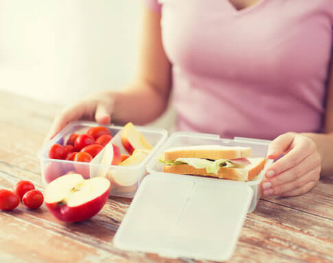 Girl in pink shirt eating healthy lunch she packed to save money during her internship