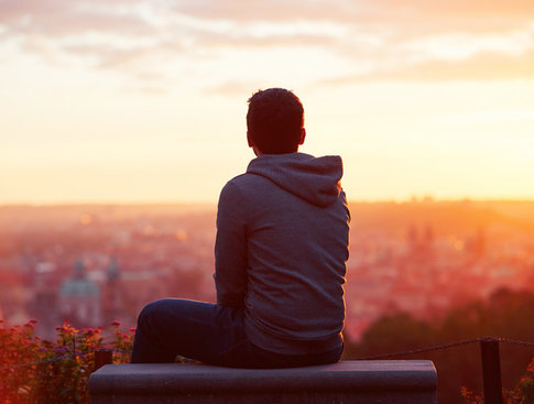 Young man looking out over a city at sunset, contemplating the concept of home