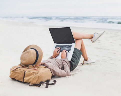 Young woman working on laptop on beach, living the life of a digital nomad