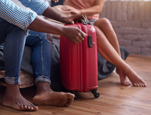 African American man and woman packing for short term move with red suitcase between them