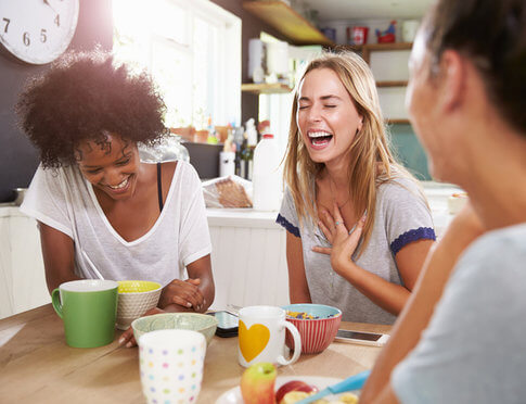 Three girl roommates laughing and enjoying breakfast together