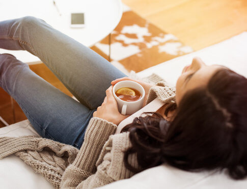 Girl relaxing in apartment on white couch with cup of hot tea