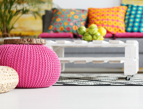 Pink pouf in foreground and colorful pillows and couch in background