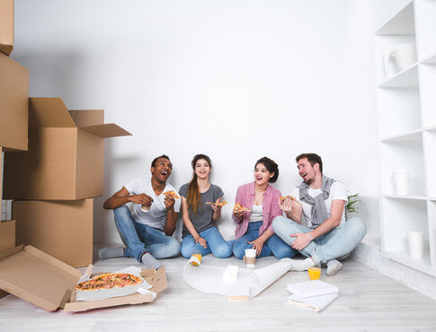 Group of friends sitting on floor of apartment after moving, eating pizza