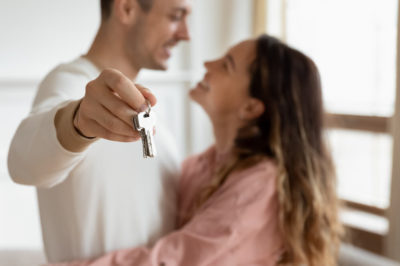 Young couple embraces as man outstretches arm holding key to new apartment.