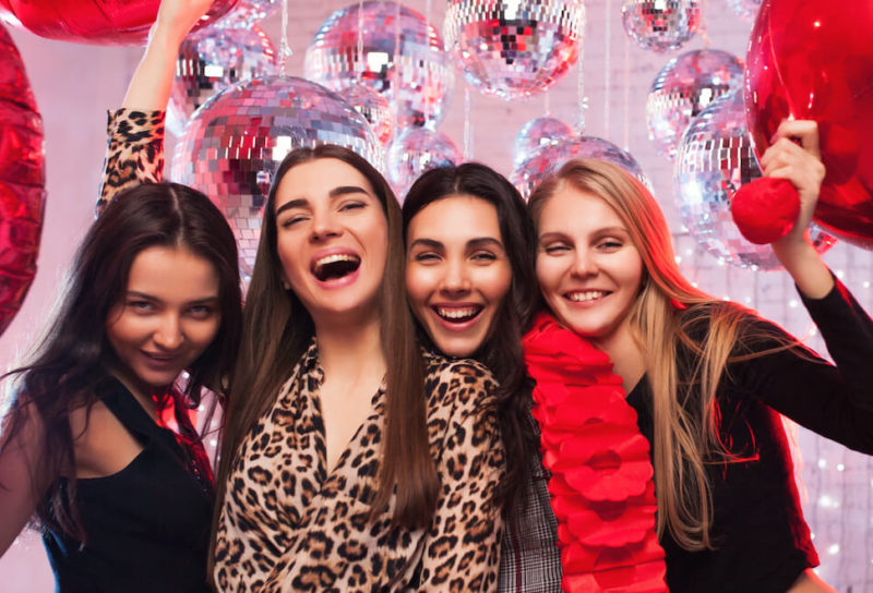 Group of young women pose together with heart balloons in Valentine's Day celebration.