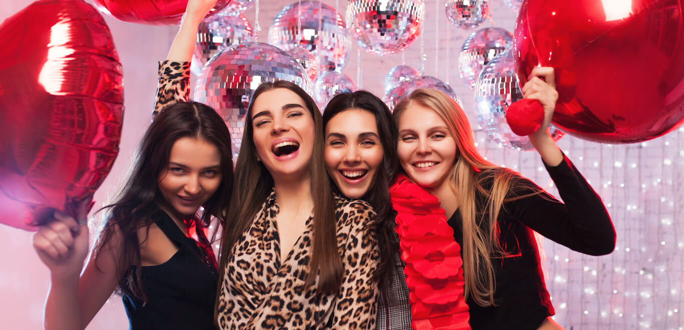 Group of young women pose together with heart balloons in Valentine's Day celebration.