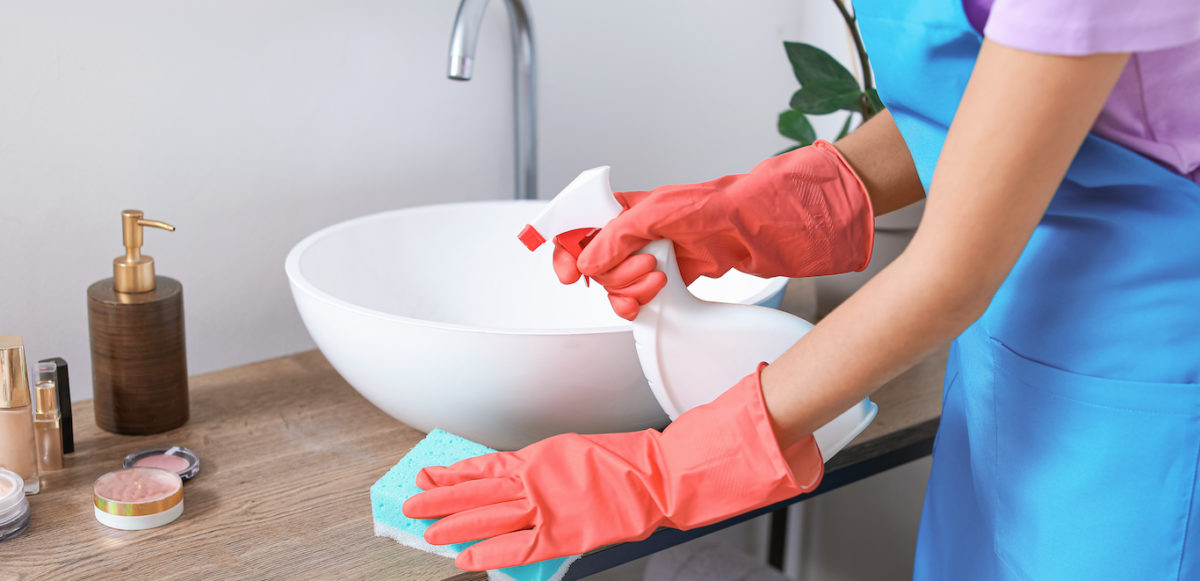 A woman in coral gloves cleans a bathroom countertop.