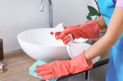 A woman in coral gloves cleans a bathroom countertop.