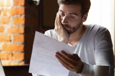 A man in a brick walled apartment sits staring disappointedly at a document.