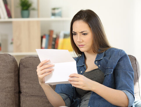 bekymret ung kvinde, der læser udsættelsesbrev på sin sofa 