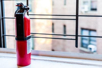 A red fire extinguisher sits in the window sill of an urban apartment.