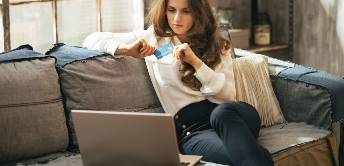 A woman looks frustrated while holding credit card and looking at laptop while sitting on the couch.