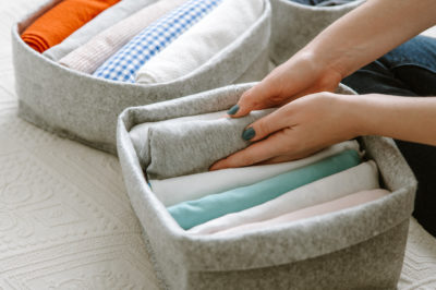 A woman's hands neatly fold clothes into soft organizational bins.