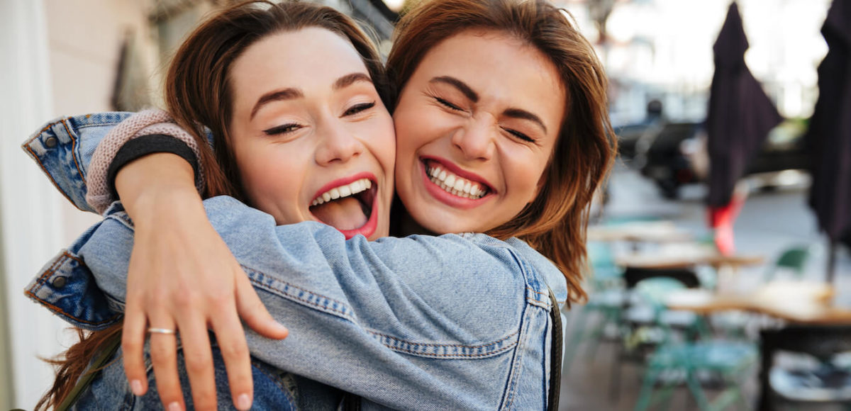 Two sisters embrace in joy on the city street.