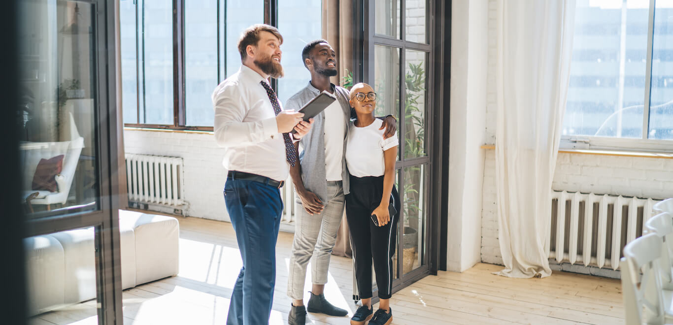 Young couple accompanied by realtor stand in modern apartment looking to lease.