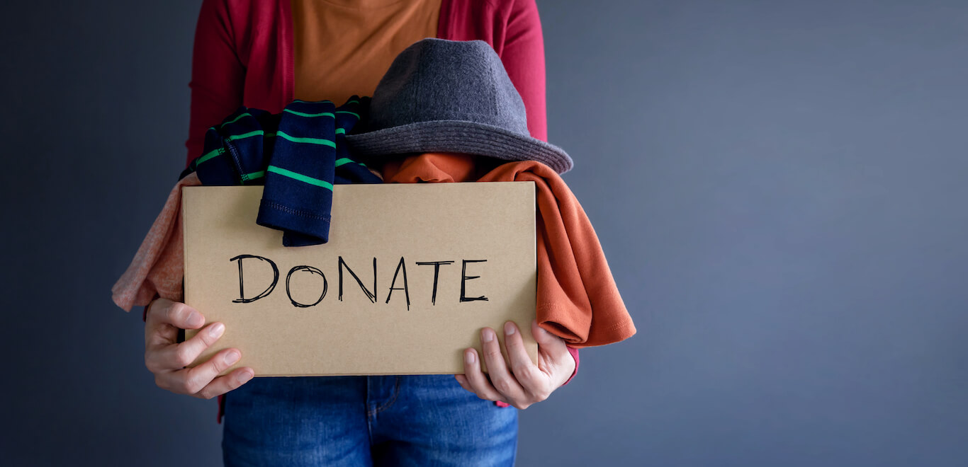 A woman clutches a cardboard box labeled "donate" filled with clothes and accessories.