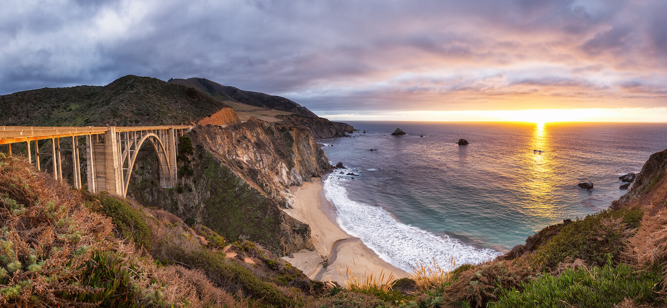 Landscape shot of Bixby Creek Bridge on Highway One overlooking ocean and sunset.