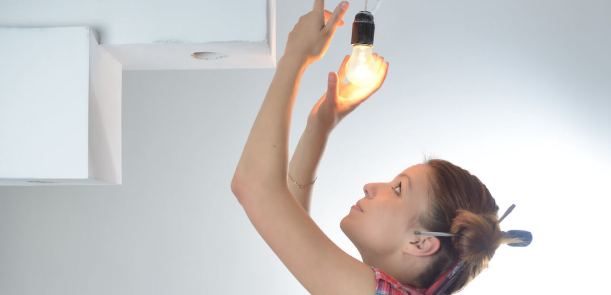 Young woman in red and blue plaid shirt screws in lightbulb.