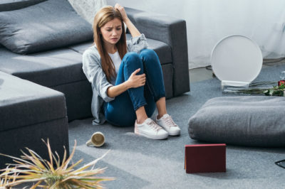 Young woman sits distressed in living room surrounded by out of place furnishings following a robbery.