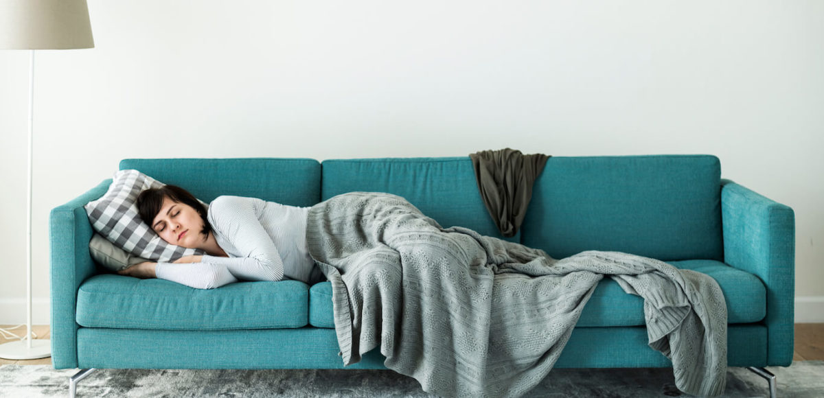 Young woman sleeps on teal couch covered in blankets.