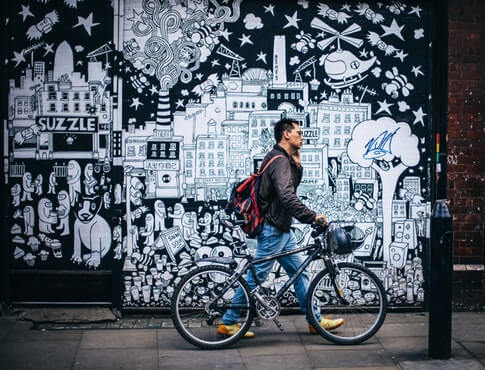 man walking his bike on sidewalk with street art