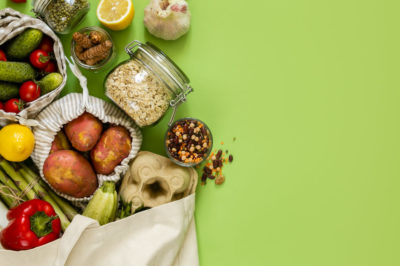 An assortment of groceries spill from a reusable bag onto a green surface.