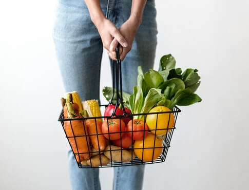 Woman wearing jeans holding a shopping basket filled with colorful fruits and veggies