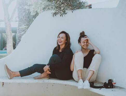two friends laugh while sitting on outdoor bench